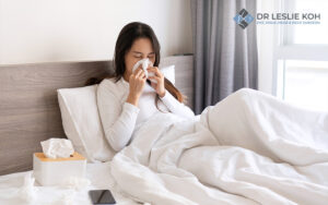 woman in bed blowing her nose on tissue