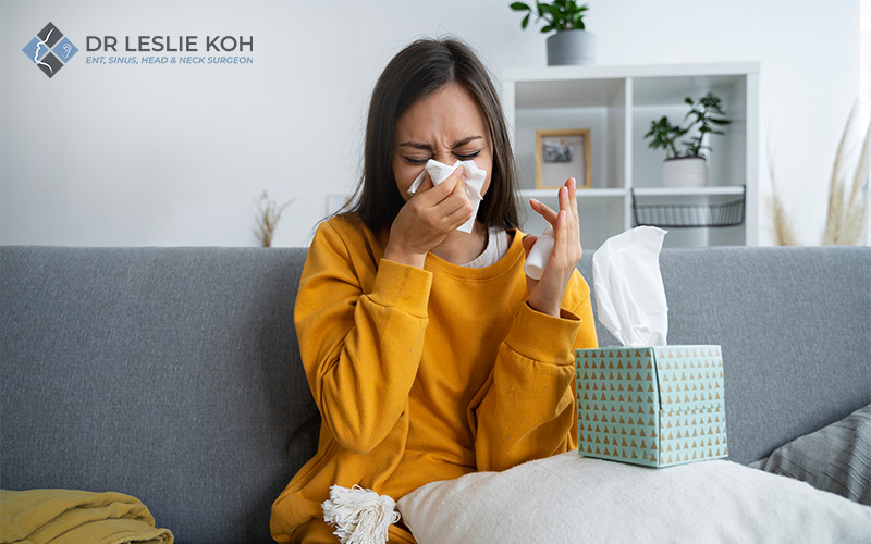 woman sitting on sofa blowing her nose on tissue