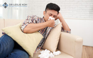 man on couch with a tissue pile in front of him blowing his nose